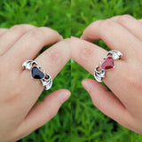Two hands wearing colorful gemstone couple rings against a green background