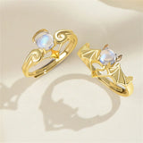 Gold couple rings with wing design and moonstone accents on beige background