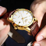 Gold case white dial watch with brown leather strap worn on wrist with a suit sleeve