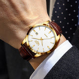 Gold case white dial watch with brown leather strap worn on wrist against a navy tie