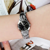Silver steel watch with black dial worn on wrist with a floral patterned sleeve