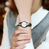 Silver steel watch with black dial worn on wrist beside a hand wearing a ring