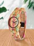 Colorful bamboo wood watch shown at an angle beside green leaves