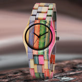 Colorful rainbow bamboo wood watch with round black dial resting on a stone surface