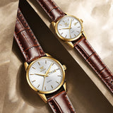 Gold white dial couple watches with brown leather straps resting on wooden surface