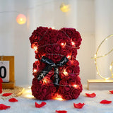 Deep red rose flower bear with black ribbon bow lit by string lights