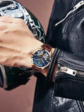 Man's wrist wearing blue dial skeleton automatic watch with denim jacket cuff