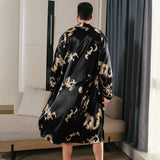 Man wearing a black silk robe with gold dragon embroidery standing by a window