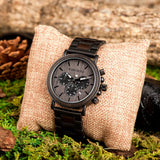 Dark wood chronograph watch resting on a burlap cushion with pine cones