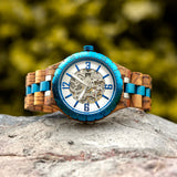 Matching his and hers wooden watches with blue accents resting on a stone outdoors