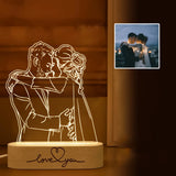Etched acrylic photo lamp of a couple glowing warm yellow against a dark wall