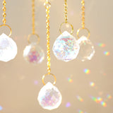 Close-up of clear faceted crystal teardrops hanging on gold chains in soft light