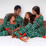 Family wearing matching green Fair Isle Christmas pyjamas on a white bed