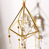 Brass diamond frame suncatcher with hanging crystal beads and shadow cast on white wall