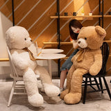 Beige giant teddy bear with satin bow tie seated beside a woman