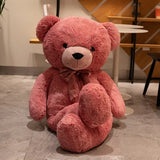 Dusty pink giant teddy bear with satin bow tie seated on a cafe floor
