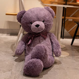 Purple giant teddy bear with satin bow tie seated on a cafe floor