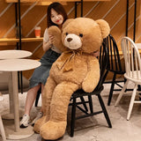 Woman leaning on a giant tan teddy bear seated on a chair for size reference