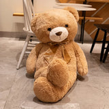 Tan giant teddy bear with satin bow seated at an angle on a floor