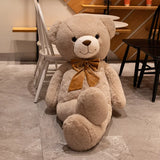 Tan giant teddy bear with gold satin bow tie seated on a floor