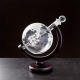 Empty etched globe decanter with glass stopper on wood base against black background