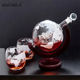Globe decanter with two etched world map tumblers on a dark surface