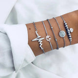 Gold layered bracelet stack with disc and heart charms worn on a wrist
