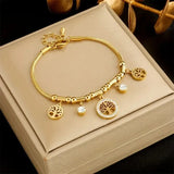 Gold bangle with small hanging charms displayed in a gift box with foliage behind