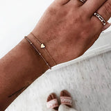 Gold layered bracelet stack with several small charms against a grey background
