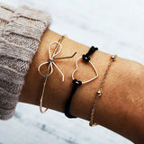 Gold bracelet stack with bow shaped bangle and beaded chains on a wrist