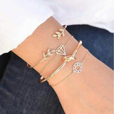 Gold chain bracelet stack with feather and leaf charms against a blue background