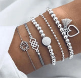 Gold and white bead bracelet stack with open heart charm on a cream sleeve
