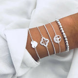 Gold layered bracelet stack with heart and round disc charms on a wrist