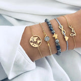 Gold bracelet stack with shell and moon charms worn on a wrist