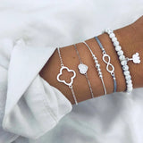 Gold chain bracelet stack with small square and geometric charms on a wrist