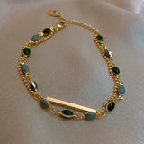 Gold bracelet set with green stones and a bar link, shown on a gift box
