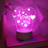 Heart LED night light glowing pink on a desk beside a book and pale wall