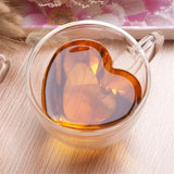 Heart shaped double wall glass cup filled with amber colored drink on wooden table