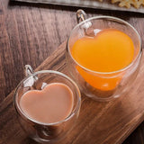 Two heart shaped double wall glass cups filled with orange and brown beverages