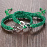 Pair of green braided rope infinity bracelets on a wooden surface