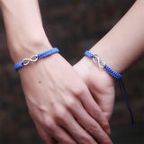 Two people clasping hands wearing matching blue infinity rope bracelets
