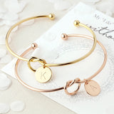 Gold and rose gold knot bangles with engraved initial disc charms on a white surface