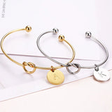 Gold, silver and rose gold knot bangles with initial coin charms side by side