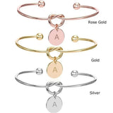 Rose gold, gold and silver knot bangles with initial disc charms shown stacked