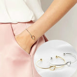 Rose gold knot bangle with engraved initial disc worn on a wrist
