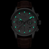 Chronograph watch photographed in darkness showing green glowing hands and hour markers