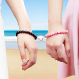 Couple's magnetic bead bracelets worn on two wrists against a beach backdrop