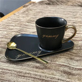 Matte black mug with gold "yummy" script and gold spoon on a matching black tray