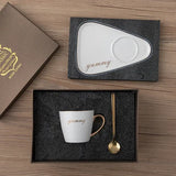 White tray and saucer set shown beside black mug with gold script and spoon