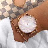 Hand holding rose gold mesh watch with pale pearl dial over a checked surface